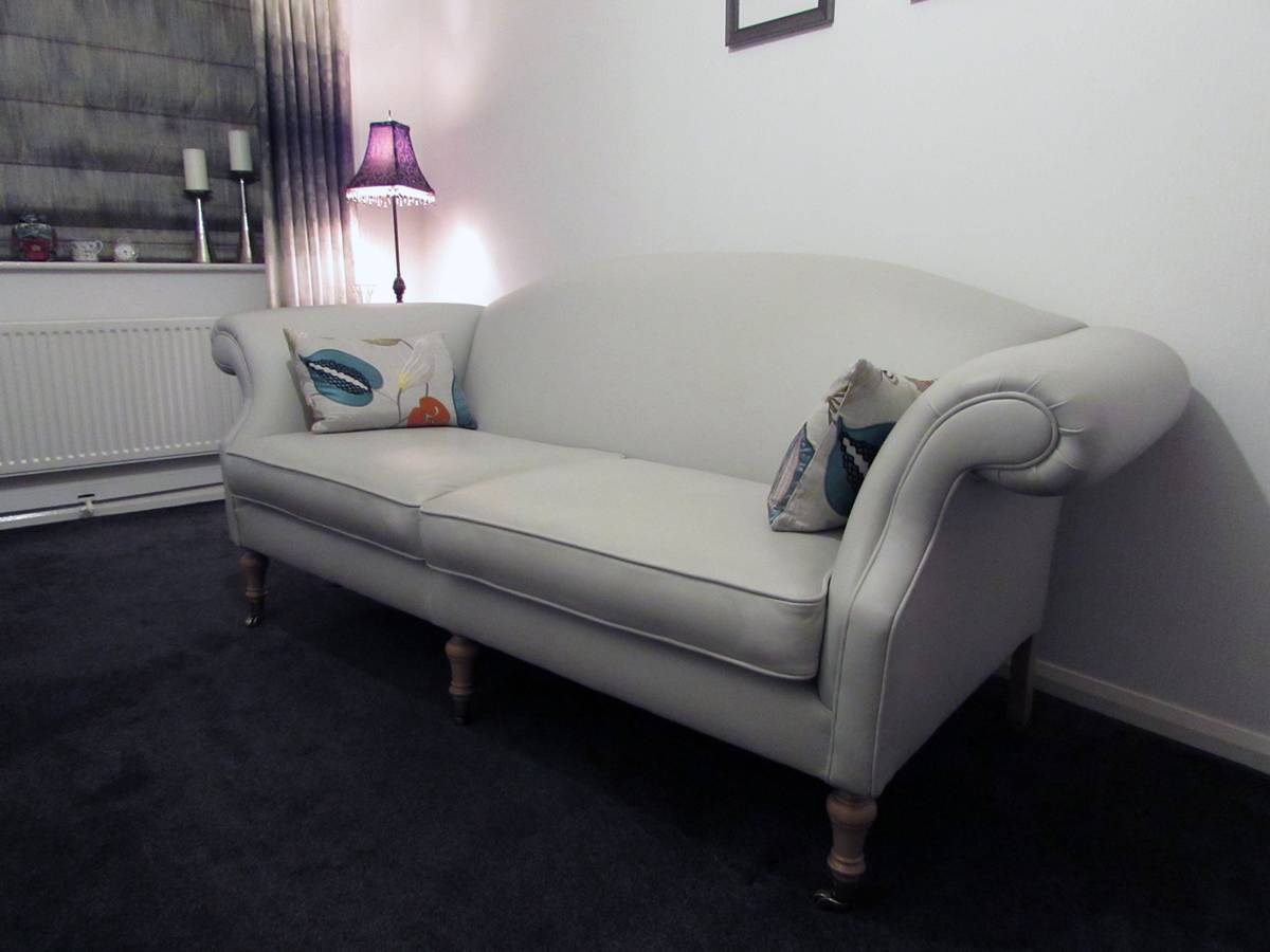 Cream leather camelback settee with scrolled arms and turned legs